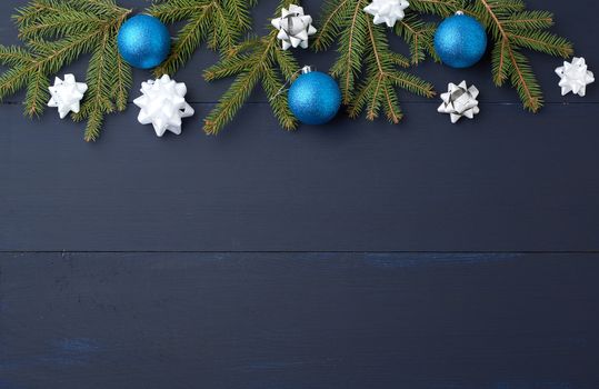 green spruce branches and dark blue shiny Christmas balls on a blue wooden background from boards, festive backdrop for Christmas and New Year, place for an inscription