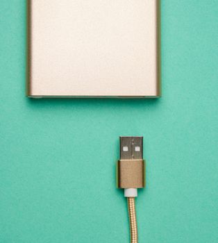 golden power bank and cord with a usb connector for recharging mobile devices on a green background, top view
