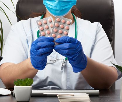 female hand with blue sterile gloves holds a stack of pills in a blister, concept for drug treatment of diseases, doctor sits in an armchair at a desk, office