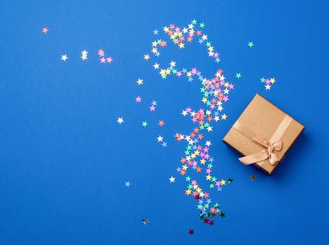 closed square golden gift box on a blue background, near multi-colored sequins, top view, festive backdrop