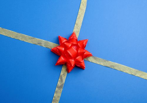 shiny golden silk ribbon crossed on a blue background in the middle of a red bow, imitation of tying a gift, top view