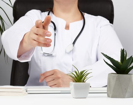 medic in a white coat sits at a table, pulls his right hand forward for a handshake, concept of receiving patients in the office