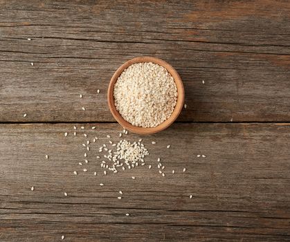 dry white sesame seeds in a brown wooden bowl on a gray wooden table from old boards, top view