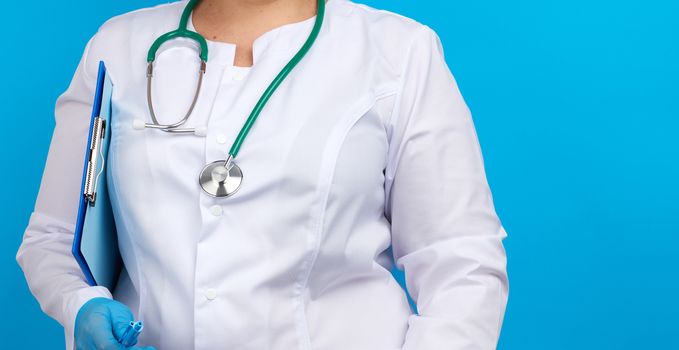 medic woman in white coat, blue latex gloves holding a tablet with a clip for papers, blue background, place for an inscription