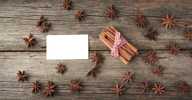 blank white business visiting card and brown cinnamon sticks tied in a bun on a gray wooden background, tasty and fragrant spice, top view