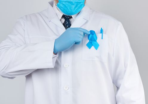 male doctor in a white coat and tie stands. On the pocket pinned a blue ribbon in the shape of a loop, symbol of the fight and treatment of prostate cancer