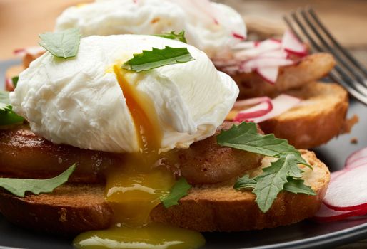 sandwich on toasted white slice of bread with poached eggs, green leaves of arugula and radish, morning breakfast on a brown wooden board, close up