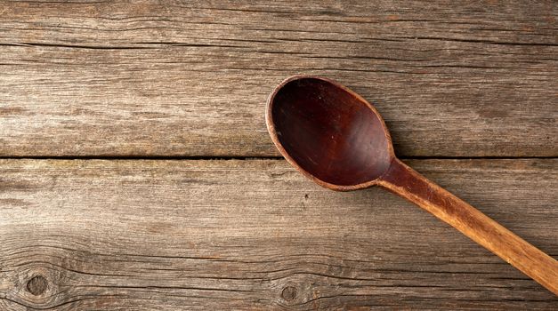 old empty brown wooden spoon on a gray wooden surface from old boards, top view