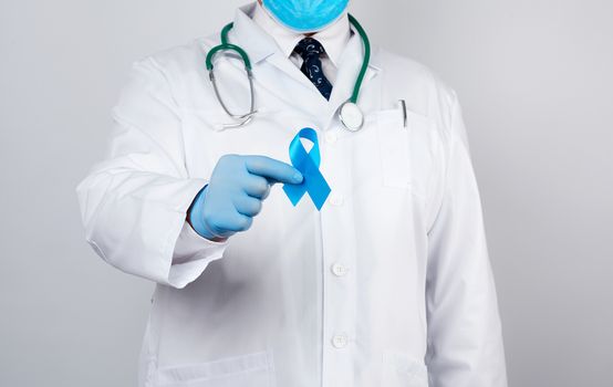 male doctor in a white coat and tie stands and holds a blue silk ribbon in a loop, wearing blue sterile medical gloves, symbol of the fight and treatment of prostate cancer