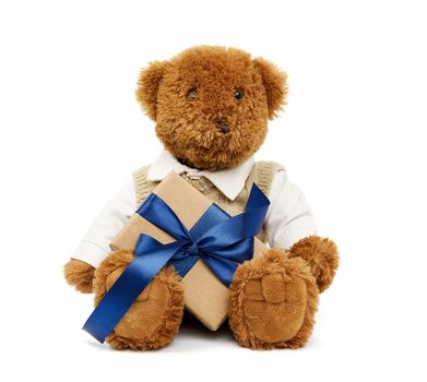 brown teddy bear sits on an isolated white background and holds a box wrapped in brown kraft paper and tied with a blue silk ribbon, festive backdrop