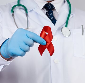 doctor in sterile latex gloves holds a red ribbon-symbol of the fight against disease AIDS and vasculitis, close up
