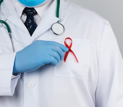 doctor in a white coat and tie is standing on a white background, red silk ribbon is hanging on his chest, symbol of the fight against disease AID