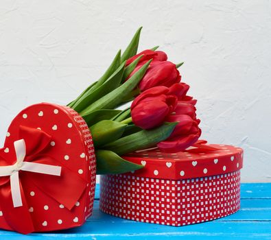 bouquet of red blooming tulips with green leaves, wrapped gifts on a blue wooden background. Festive backdrop for birthday, Valentine's day, anniversary