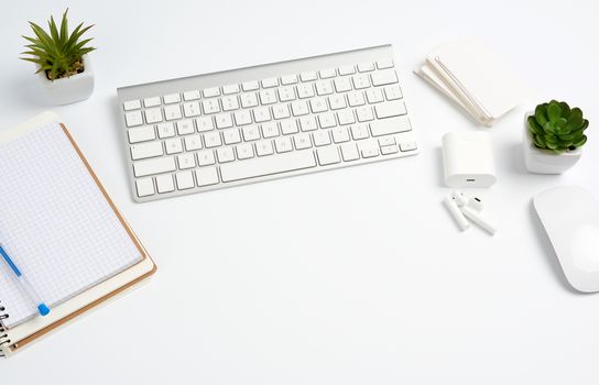 White wireless keyboard, a stack of notebooks, green plants in pots and a mouse, workplace of a freelancer, businessman. White table