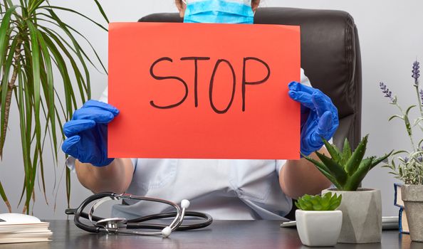 female medic is sitting in a brown leather chair in the office holding a red sheet of paper with the words stop, concept is not to panic, keep calm