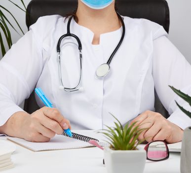 woman doctor in a white coat writes a prescription on a form, therapist sits on a chair at a white table, workplace