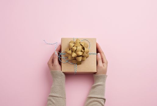 female hand holds a square box with a bow on a pink background, concept of a congratulation on a happy birthday