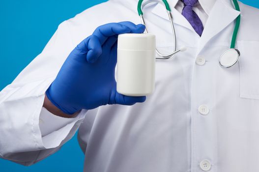 male hand in blue sterile gloves holds a white plastic jar for pills, medical treatment concept for diseases, blue background