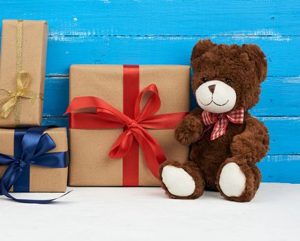 cute brown teddy bear sits on a blue wooden background, bouquet of red tulips and gift box, festive backdrop for birthday, Valentine's day, anniversary