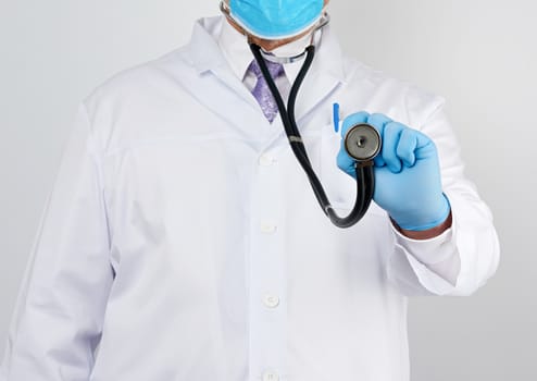 doctor in a white coat and tie holds in his hand a black phonendoscope, wearing blue sterile gloves, white background