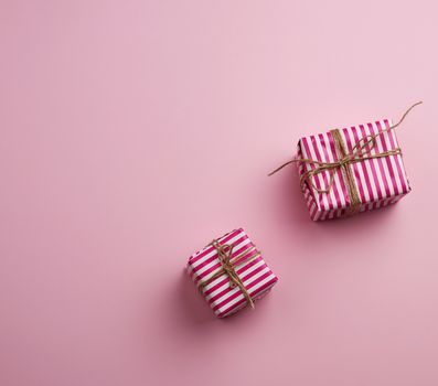 two gifts wrapped in pink striped paper on a pink background, top view, copy space