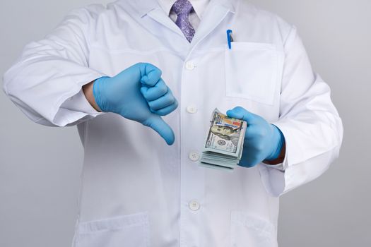 doctor in blue uniform and latex gloves keeps one hand a lot of money, other hand shows a bad gesture, concept of a bribe 