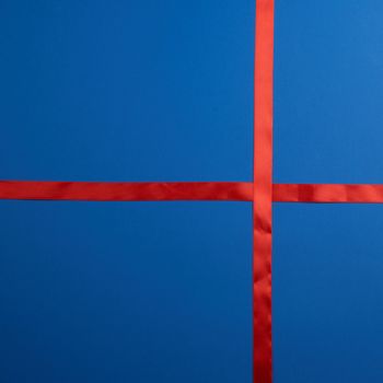red silk ribbon crossed on a dark blue background, imitation of tying a gift, top view