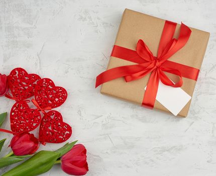 bouquet of red blooming tulips with green leaves, wrapped gift in brown craft paper on a white background. Festive backdrop for birthday, Valentine's day