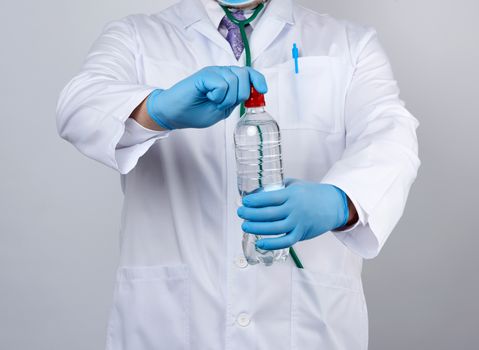 doctor in a white coat and blue latex gloves holds a transparent bottle of water, human consumption concept