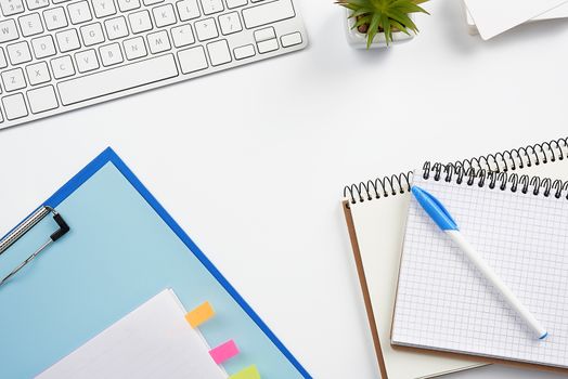 White wireless keyboard, a stack of notebooks, green plants in pots and a mouse, workplace of a freelancer, businessman. White table