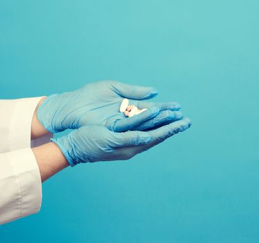 hand with blue sterile gloves holds round pink pills, concept of drug treatment for diseases, blue background