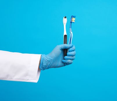 doctor therapist is dressed in a white robe uniform and blue sterile gloves holding a toothbrush, daily brushing concept, blue background