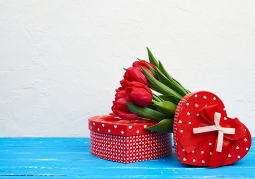 bouquet of red blooming tulips with green leaves, wrapped gifts on a blue wooden background. Festive backdrop for birthday, Valentine's day, anniversary