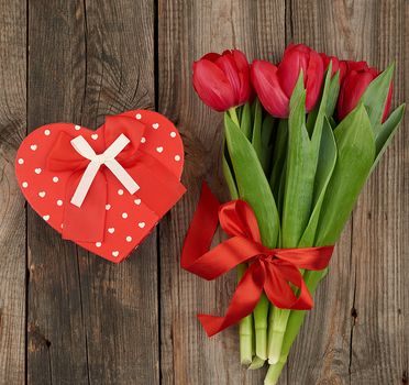 bouquet of red blooming tulips with green leaves, wrapped gifts on a gray wooden background. Festive backdrop for birthday, Valentine's day, anniversary