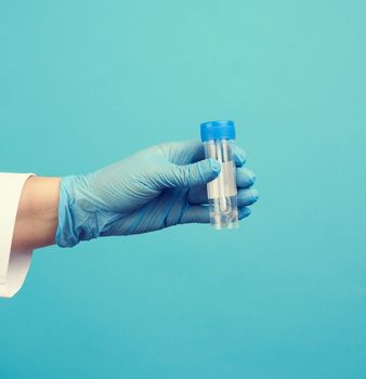 doctor in a white coat and blue sterile latex gloves holds a plastic jar for stool analysis, blue background