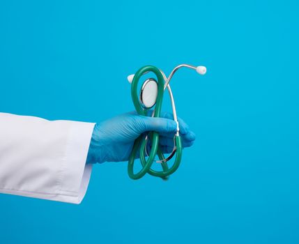 doctor in a white medical coat holds a black stethoscope on a blue background, close up
