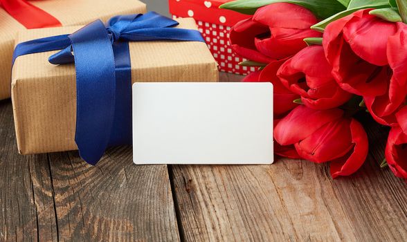 empty rectangular white paper business card, a bouquet of red tulips and wrapped gifts on a gray wooden table. Festive backdrop for birthday, Valentine's day, anniversary