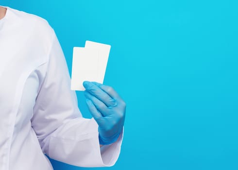 doctor hand in blue medical latex gloves holds an empty paper business card on a blue background, place for an inscription