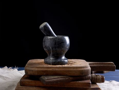 black stone mortar with pestle for grinding spices and herbs on a brown wooden board, black background