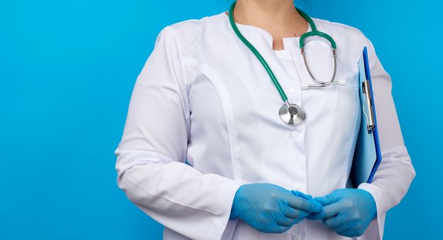 medic woman in white coat, blue latex gloves holding a tablet with a clip for papers, blue background, place for an inscription