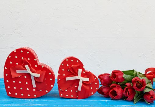 bouquet of red blooming tulips with green leaves, wrapped gifts on a blue wooden background. Festive backdrop for birthday, Valentine's day, anniversary