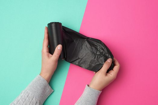 female hand unwinds a black plastic bag for rubbish, green pink background, top view