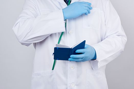male doctor in a white coat with buttons, wearing blue sterile gloves, holding a open blue paper notebook in his hand on a white studio background