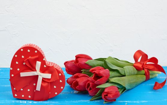 bouquet of red blooming tulips with green leaves, wrapped gifts on a blue wooden background. Festive backdrop for birthday, Valentine's day, anniversary