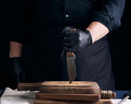 chef in a black shirt and black latex gloves holds a vintage kitchen knife for cutting meat, low key