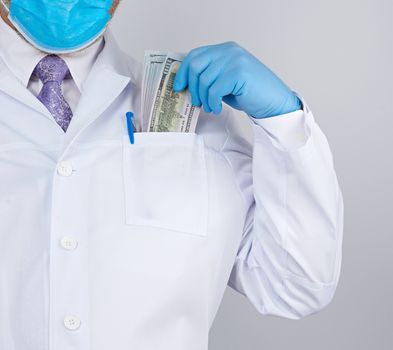 physician in a white coat, wearing blue sterile gloves, doctor holds a pack of paper money, anti-corruption concept, bribe and payment for the work done