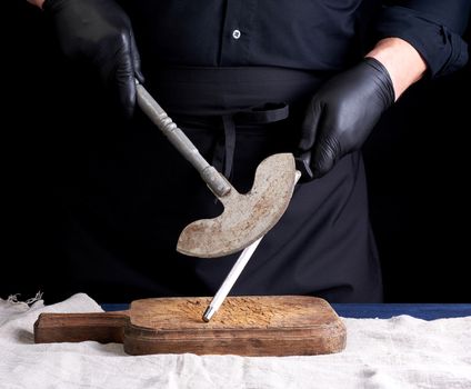 male cook in black uniform and black latex gloves holds a large sharp vintage knife for meat and vegetables and a metal sharpener for knives, black background