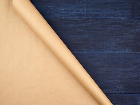 untwisted roll of brown craft paper on a blue wooden background, empty space. Old craft paper texture. Clean sheet, template, angle is twisted
