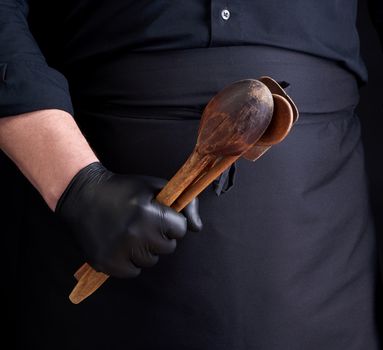 chef in black latex gloves and a black uniform holds wooden vintage spoons in front of him, low key