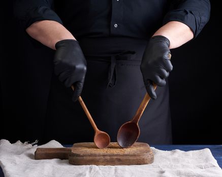 chef in black latex gloves and a black uniform holds wooden vintage spoons in front of him, low key
